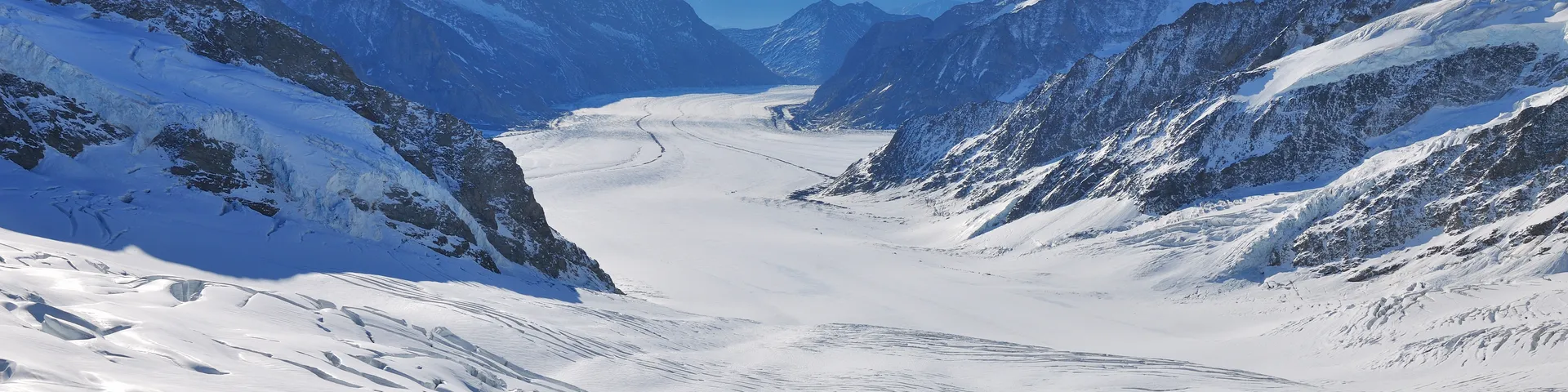 Paesaggio costituito da un ampio ghiacciaio circondato da montagne innevate che si perde in lontananza, sotto un cielo limpido e azzurro.