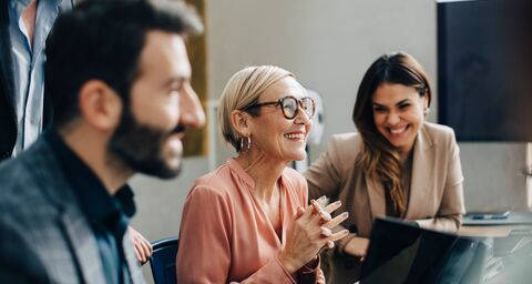 Ein Mann und zwei Frauen sitzten in einem Office und lachen.