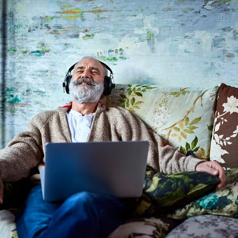An elderly gentleman relaxing on the sofa and listening to music through headphones