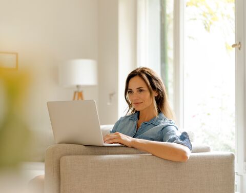 A women is sitting at home in front of her laptop with her cat