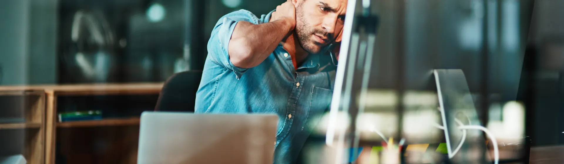 Un uomo è seduto a una scrivania davanti allo schermo di un computer e si massaggia il collo, evidentemente stressato o teso.