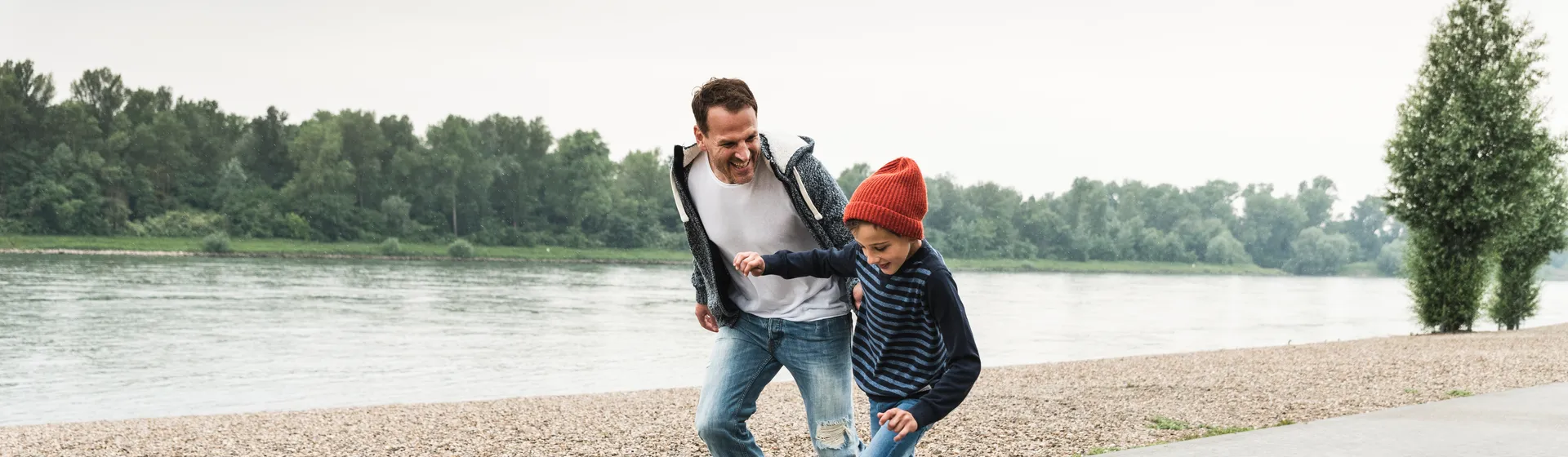 Un père et son fils font du skateboard ensemble au bord d'une rivière, tout en riant et en s'amusant.