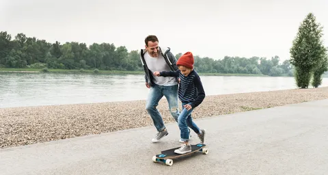 Sohn draussen auf dem Skateboard und sein Verter hält ihn. 