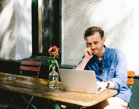A man is working on his laptop outside at the garden table.